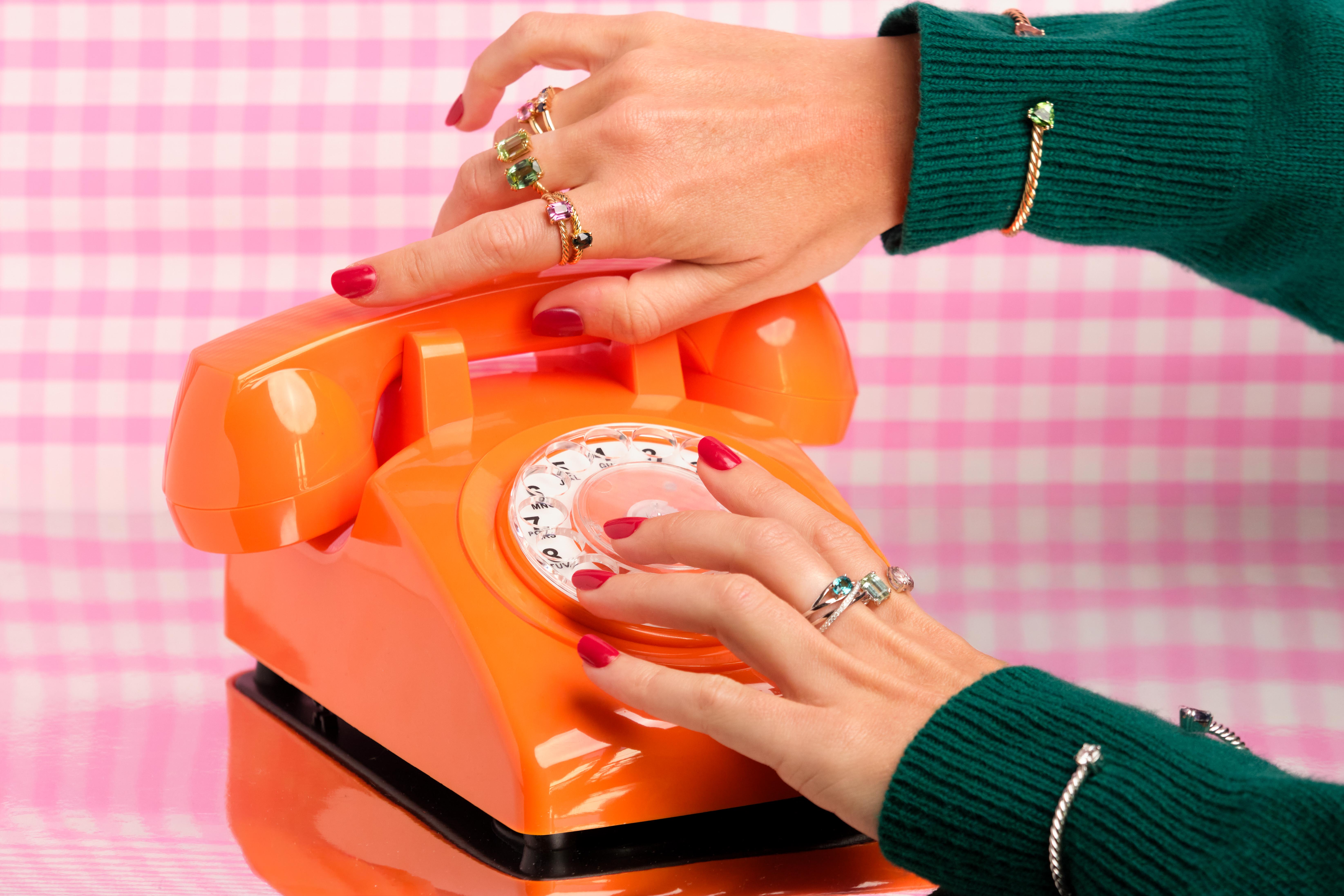 visual of hands hanging a orange telephone with high jewelry rings